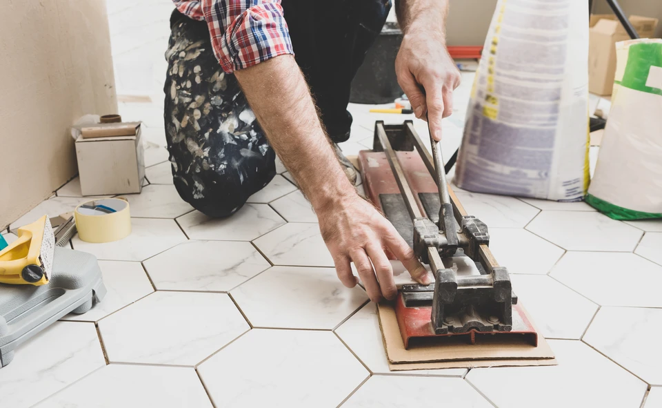 Ouvrier en combinaison bleue et casque jaune utilisant une scie circulaire &eacute;lectrique pour d&eacute;couper du carrelage dans un chantier de r&eacute;novation int&eacute;rieure
