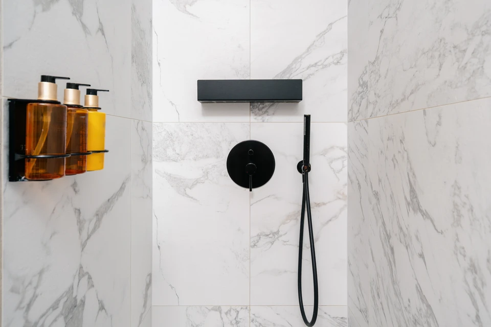 Ouvrier en casquette applique de l'adhésif de carrelage sur mur intérieur avec spatule crantée, tenant carreau gris dans l'autre main