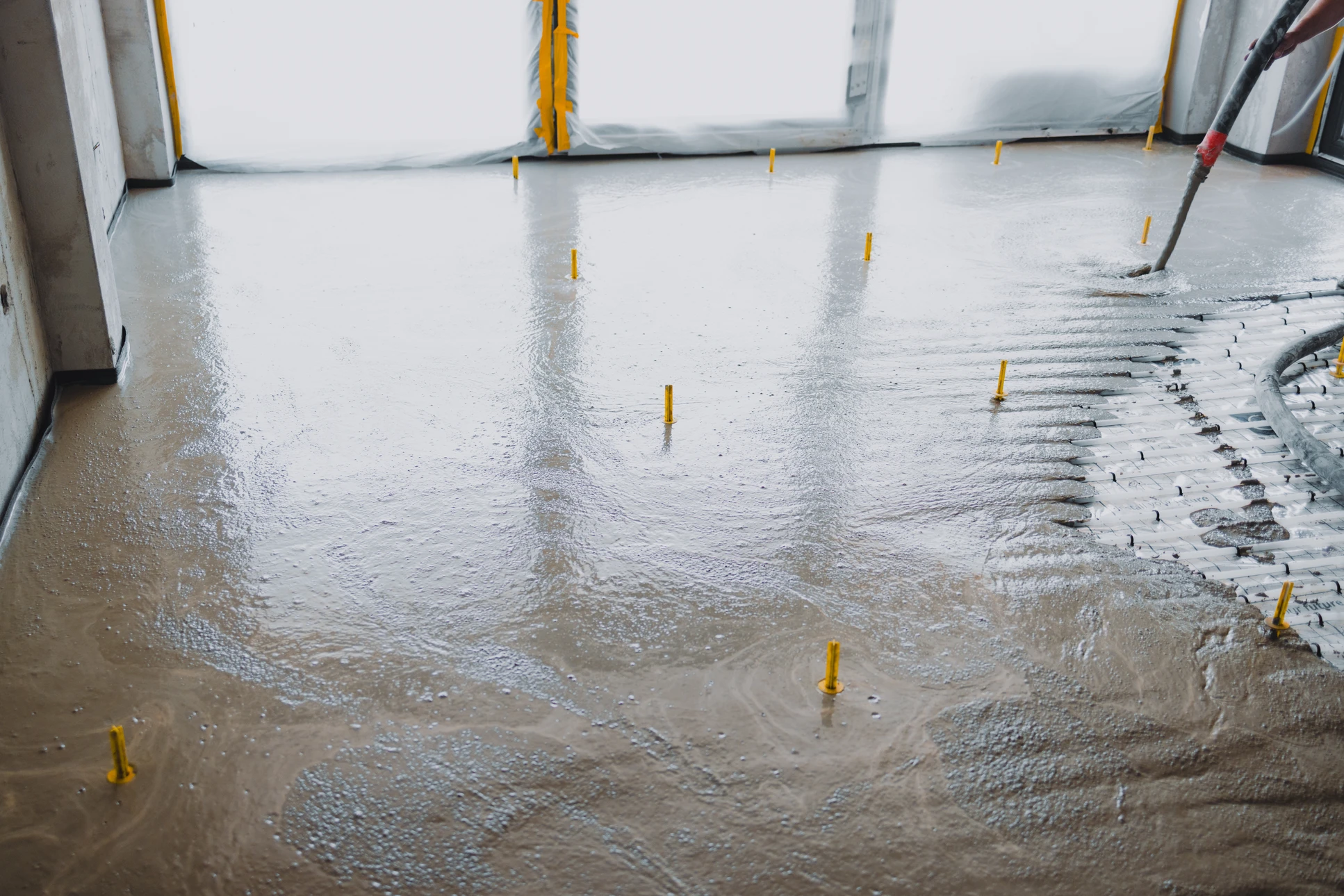 Chantier extérieur de construction avec ouvrier en casque orange appliquant du béton frais sur dalle armée